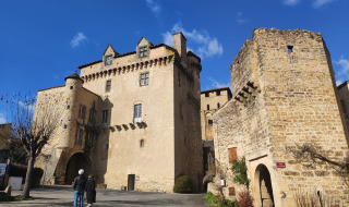 Dos personas caminan hacia un castillo de piedra histórica bajo cielo azul cerca de Varen, Occitanie, Francia.