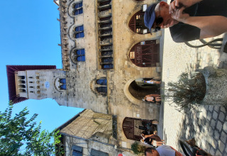 Mand sidder udenfor ved Le Camp i Occitanie, Frankrig, med historisk stenbygning i baggrunden.