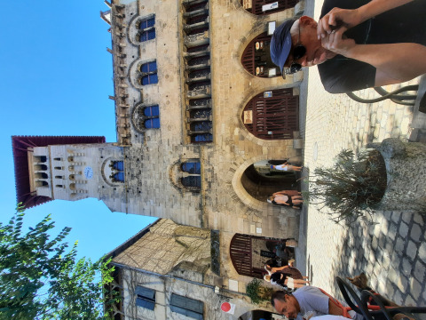 Man sits outside at Le Camp in Occitanie, France, with a historic stone building in the background.
