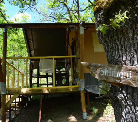 Tienda safari Shimoni en Eco domaine Le Camp, Francia, rodeada de árboles y terraza de madera rústica.