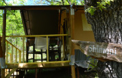 Tienda safari Shimoni en Eco domaine Le Camp, Francia, rodeada de árboles y terraza de madera rústica.