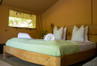 Interno di una tenda safari con letto in legno, coperta verde e asciugamani bianchi arrotolati.