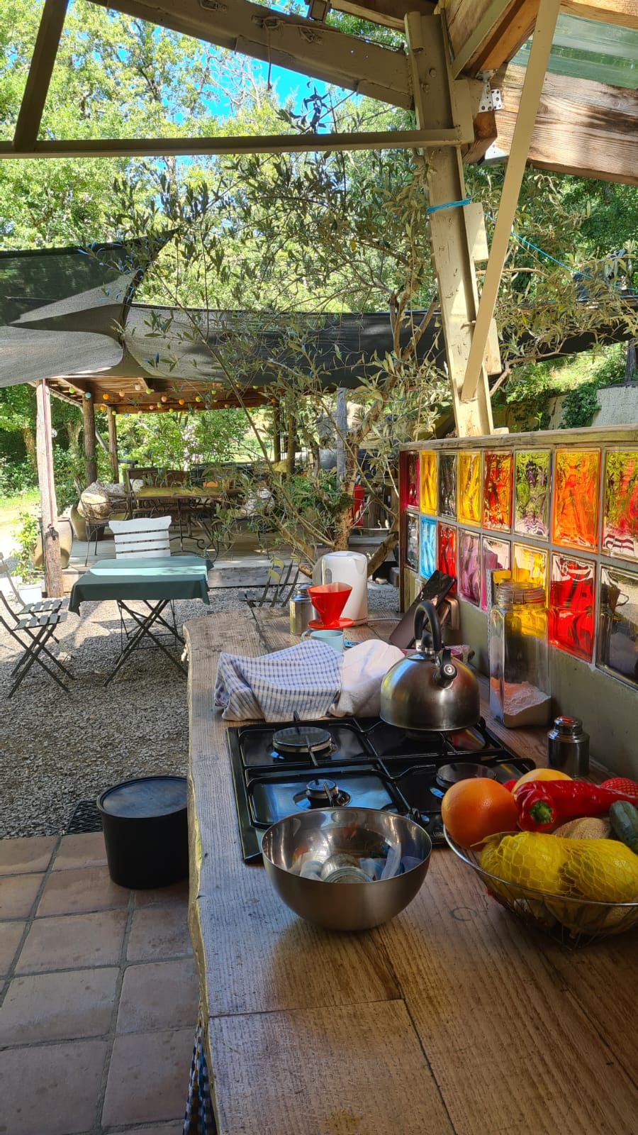 Buitenkoken bij safaritent met fruit, fornuis, gekleurde ramen en tafels onder schaduwdoeken.