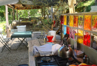 Outdoor kitchen at safari tent, with fruit, stove, colorful windows, and tables under shade trees.