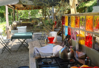 Cuisine extérieure de tente safari avec fruits, gazinière, vitraux et tables sous les arbres.