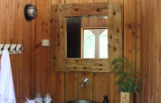 Baño de tienda safari con paredes de madera, espejo rústico, lavabo metálico y planta decorativa.