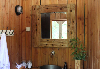 Baño de tienda safari con paredes de madera, espejo rústico, lavabo metálico y planta decorativa.