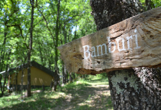 Cartello di legno con scritto 'Bamburi' vicino a una tenda safari all’Eco domaine Le Camp, Francia, bosco.