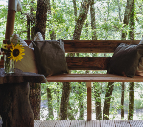 Panca in legno con cuscini e girasoli in vaso su terrazza tra gli alberi di Tent Bamburi, Eco domaine Le Camp, Francia.
