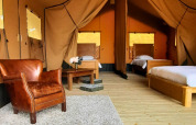 Intérieur de la tente safari Lodgetent Chrysalide à l’Eco domaine Le Camp, France, avec lits et fauteuil en cuir.