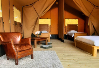 Interior de la tienda safari Lodgetent Chrysalide en Eco domaine Le Camp, Francia, con camas y sillón de cuero.