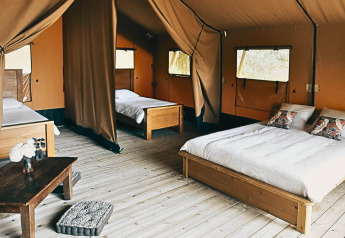 Gemütliches Safari-Lodgetent mit Holzboden, Doppelbett, Einzelbetten und Fenstern im Eco Domaine Le Camp.