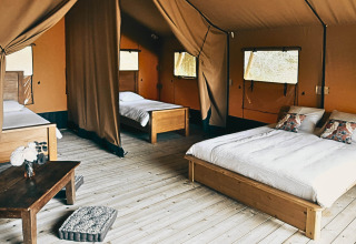 Luksuriøs safari-lodgetelt med trægulv, dobbeltseng, enkeltsenge og naturlig belysning i Frankrig.