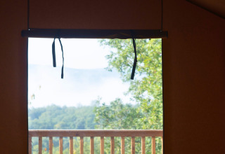 Blick aus dem Lodgetent Chrysalide im Eco domaine Le Camp in Frankreich auf einen Balkon mit Natur.