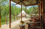 Vista da una lodge tenda safari con mobili in legno e fiori sul tavolo, immersa nel verde in Francia.