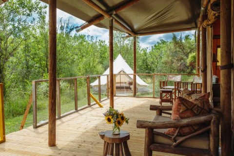 Blick von einer Safari-Zelt-Lodge mit Holzmöbeln und Blumen auf dem Tisch in grüner Natur in Frankreich.