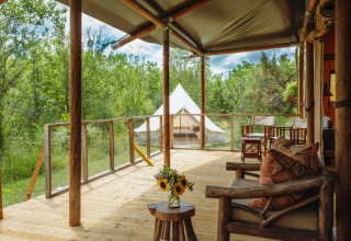 Blick von einer Safari-Zelt-Lodge mit Holzmöbeln und Blumen auf dem Tisch in grüner Natur in Frankreich.