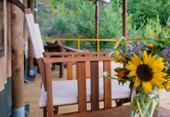 Holzterrasse mit Sonnenblumen in einer Glasvase bei Tent Lodge Maasai Mara im Eco domaine Le Camp, Frankreich.