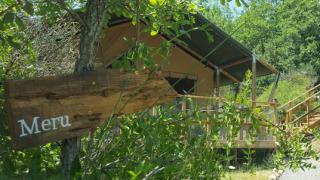Une tente safari nommée Lodgetent Meru partiellement cachée par la verdure, panneau en bois au premier plan.