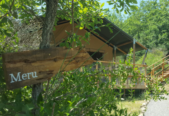 Una tienda safari llamada Lodgetent Meru, parcialmente oculta entre la vegetación y un cartel de madera delante.