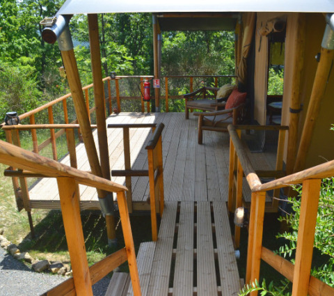 Wooden deck outside a safari lodgetent at Eco domaine Le Camp in France, surrounded by greenery.