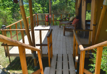 Terrasse en bois devant une tente safari au Eco domaine Le Camp en France, entourée de verdure.