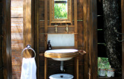Salle de bain extérieure rustique avec murs en bois, miroir, lavabo et serviette à Lodgetent Meru, Le Camp, France.