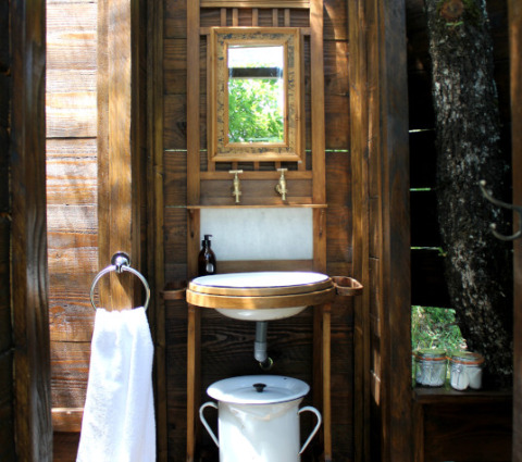 Baño exterior rústico con paredes de madera, espejo, lavabo y toalla en Lodgetent Meru, Le Camp, Francia.
