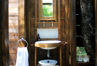 Baño exterior rústico con paredes de madera, espejo, lavabo y toalla en Lodgetent Meru, Le Camp, Francia.