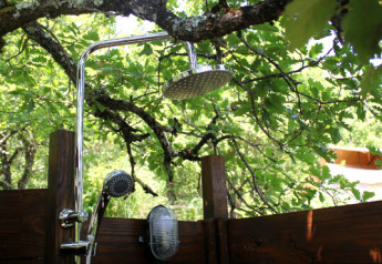 Außendusche unter Bäumen bei Lodgetent Meru, Eco domaine Le Camp, Frankreich, inmitten der Natur.
