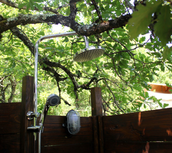 Ducha al aire libre bajo árboles en Lodgetent Meru, Eco domaine Le Camp, Francia, rodeado de naturaleza.