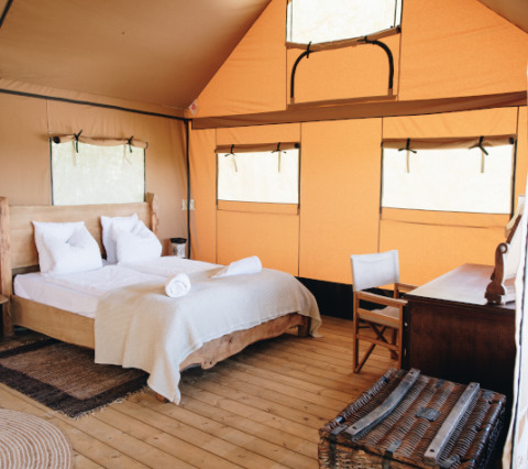 Interior of Lodgetent Samburu at Eco domaine Le Camp, France, featuring a bed, desk, and rustic decor.