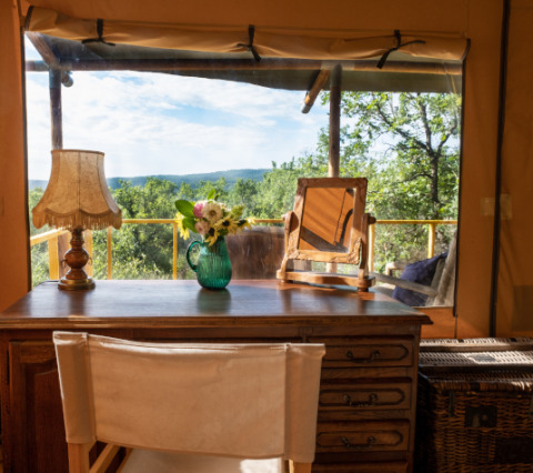 Desk with lamp, flowers, and mirror inside a safari tent with a scenic view at Le Camp in France.