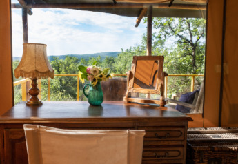 Escritorio con lámpara, flores y espejo en tienda de safari con vista panorámica en Le Camp, Francia.