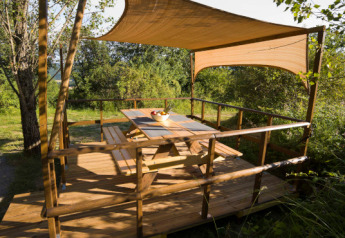 Terrasse en bois avec auvent à la Lodgetent Mont Kenya, Eco domaine Le Camp, France, entourée de verdure.