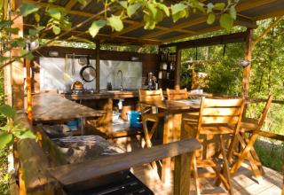 Buitenkeuken met houten tafel en stoelen onder afdak, midden in het groen op Le Camp in Frankrijk.