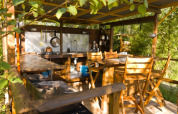 Cocina exterior rústica y zona de comedor de madera rodeada de vegetación, en Le Camp, Francia.