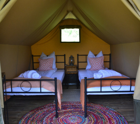 Interior de una tienda safari con dos camas individuales, mantas, cojines y alfombra colorida en Le Camp, Francia.