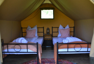 Interior de una tienda safari con dos camas individuales, mantas, cojines y alfombra colorida en Le Camp, Francia.