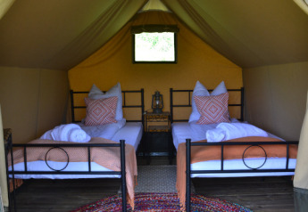 Intérieur d’une tente safari avec deux lits simples, coussins, couvertures et tapis coloré au Le Camp, France.