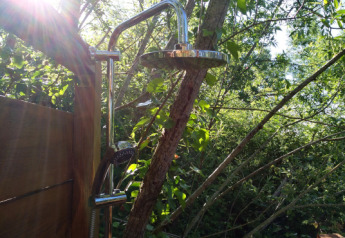 Douche extérieure du Lodgetent Mont Kenya à l’Eco domaine Le Camp, entourée d’arbres et de soleil.