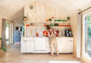 Due persone in una cucina moderna in legno chiaro con stoviglie colorate in un villaggio vacanze nelle Fiandre Occidentali.