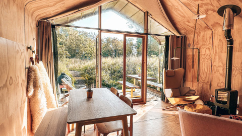 Acogedora cabaña de madera con grandes ventanales, mesa de comedor y estufa en Les Cabanes d'Ostende.