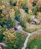 Vista aérea de cabañas pequeñas en el bosque cerca de Oostende, Bélgica, rodeadas de árboles y senderos.
