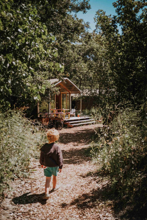 Un niño camina hacia una cabaña en Les Cabanes d'Ostende, rodeado de naturaleza en el parque de vacaciones en Flandes Occidental.