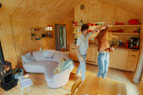 Pareja bailando contenta en una acogedora cabaña de madera en Les Cabanes d'Ostende, Flandes Occidental.