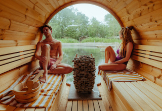 Een koppel ontspant in een barrelsauna met zicht op de natuur bij Les Cabanes d'Ostende, België.