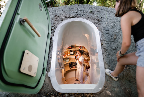 Vrouw in een ondergrondse voorraadkelder met eten en drank, gezien van buiten bij Les Cabanes d’Ostende, België.
