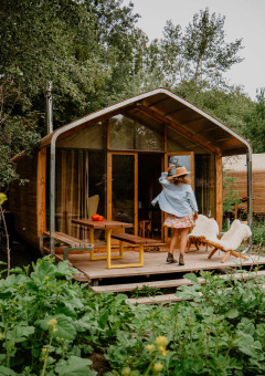 Mujer en el porche de una cabaña en Les Cabanes d'Ostende, rodeada de naturaleza en Flandes Occidental, Bélgica.