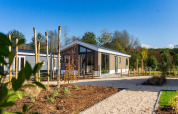 Moderne lodge ved Velthorst på Zilverstrand i Belgien, omgivet af have og træer under en klar blå himmel.